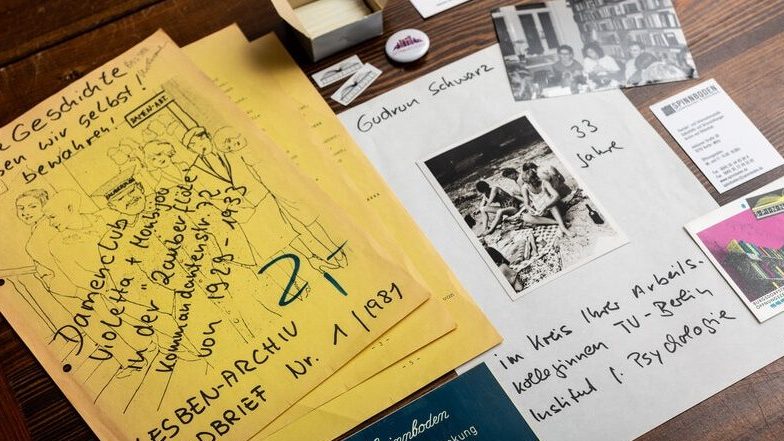 Auf dem Foto sind frühe Erzeugnisse aus der Gründungszeit des Spinnbodens abgebildet. So der erste Rundbrief von 1981 und ein Foto von Gudrun Schwar, welche das Archiv gegründet hat.